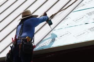 J. Carnes & Son Roofing crew member fastening standing-seam metal roof panels over GAF ice and water shield on a New Hampshire home