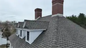 Finished gray architectural shingle roof with ridge cap, three dormers and two brick chimneys on a New Hampshire home, by J. Carnes & Son Roofing