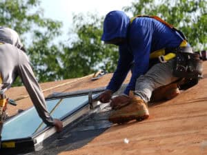J. Carnes & Son Roofing crew member in a safety harness fastening the flashing on a new VELUX skylight during a roof installation on a New Hampshire home