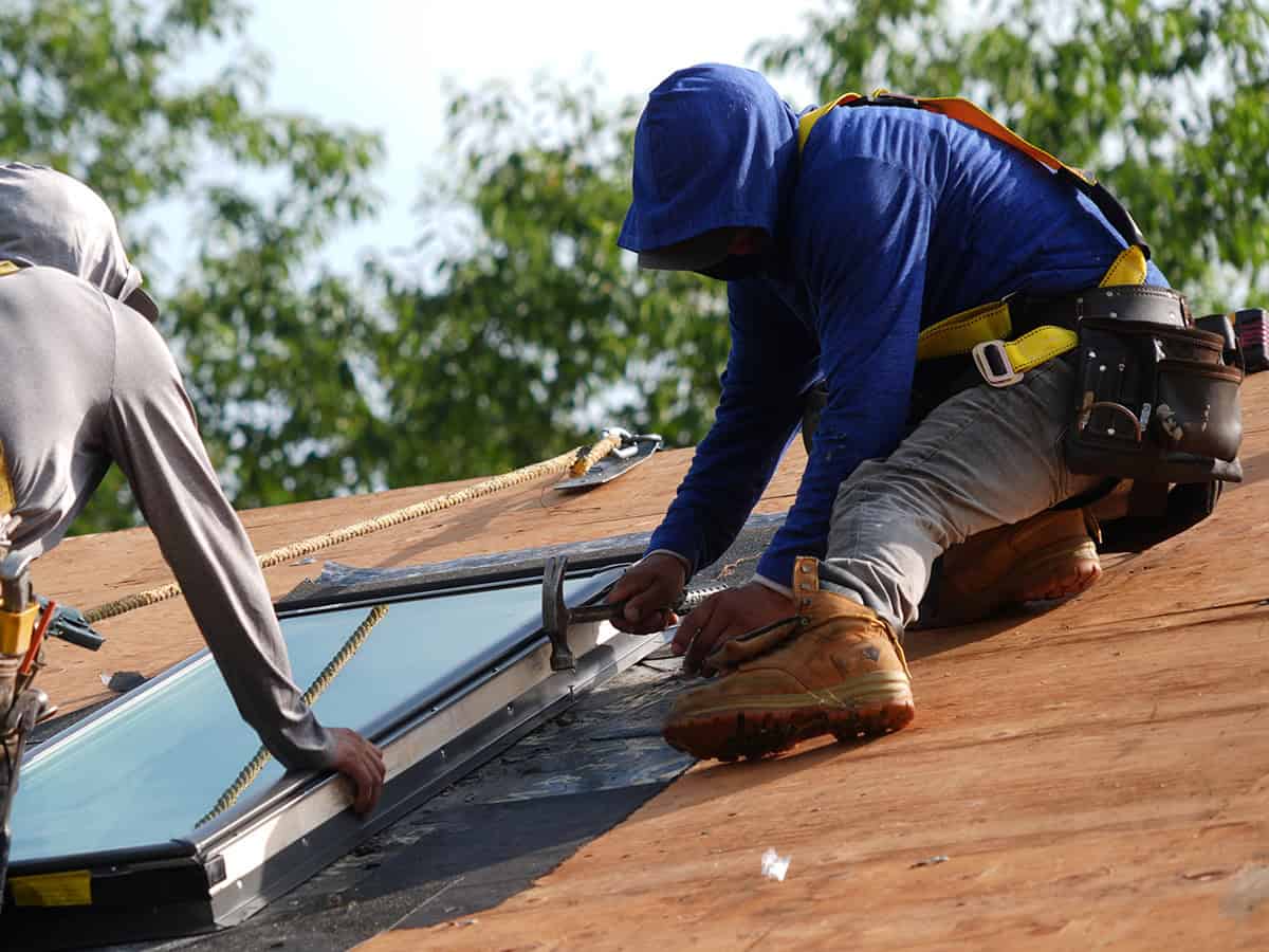 J. Carnes & Son Roofing crew member in a safety harness fastening the flashing on a new VELUX skylight during a roof installation on a New Hampshire home
