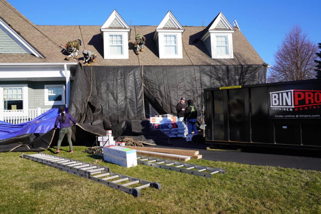 J. Carnes & Son Roofing crew tarping the siding and staging materials during a full roof replacement on a New Hampshire Seacoast home