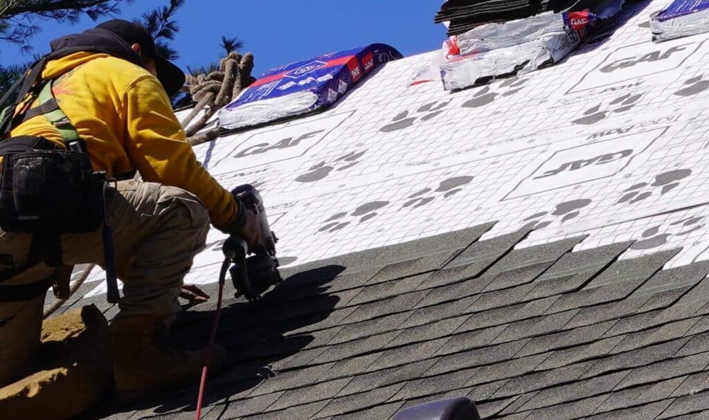 J. Carnes & Son Roofing crew member nailing architectural asphalt shingles over GAF underlayment on a New Hampshire Seacoast home