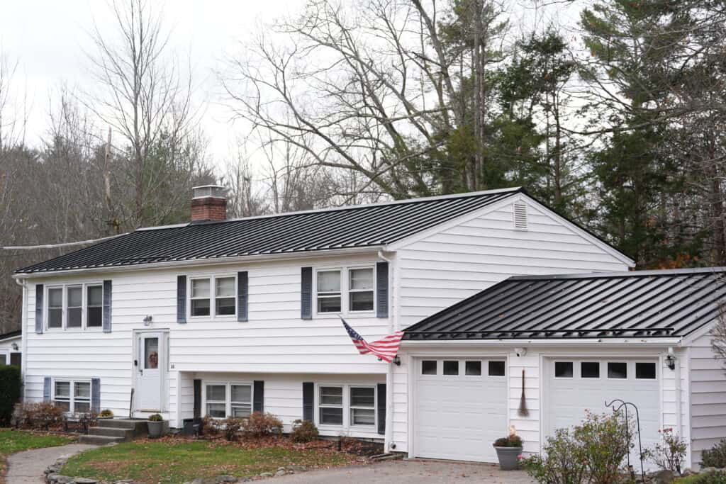 Black standing seam metal roof installed by J. Carnes & Son Roofing on a white split-level home in New Hampshire