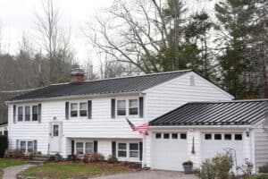 Black standing seam metal roof installed by J. Carnes & Son Roofing on a white split-level home in New Hampshire