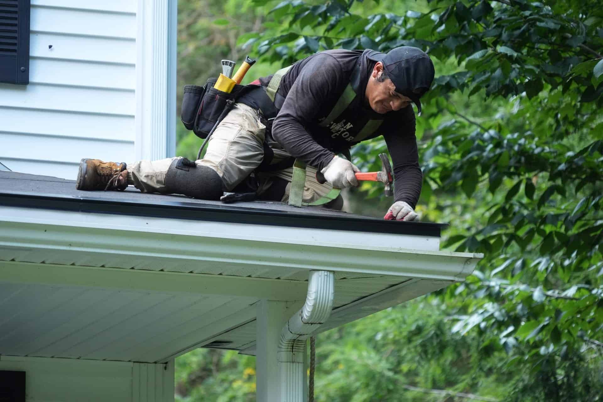 J. Carnes & Son Roofing crew member in a safety harness repairing the roof edge above the gutter on a New Hampshire home